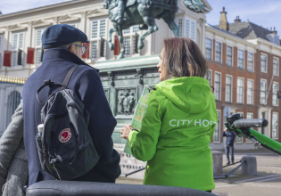 A woman in a green jacket talks to a man in a hat near the Binnenhof.