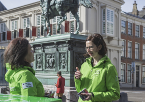 Twee vrouwen in groene jassen praten bij een standbeeld in Den Haag.