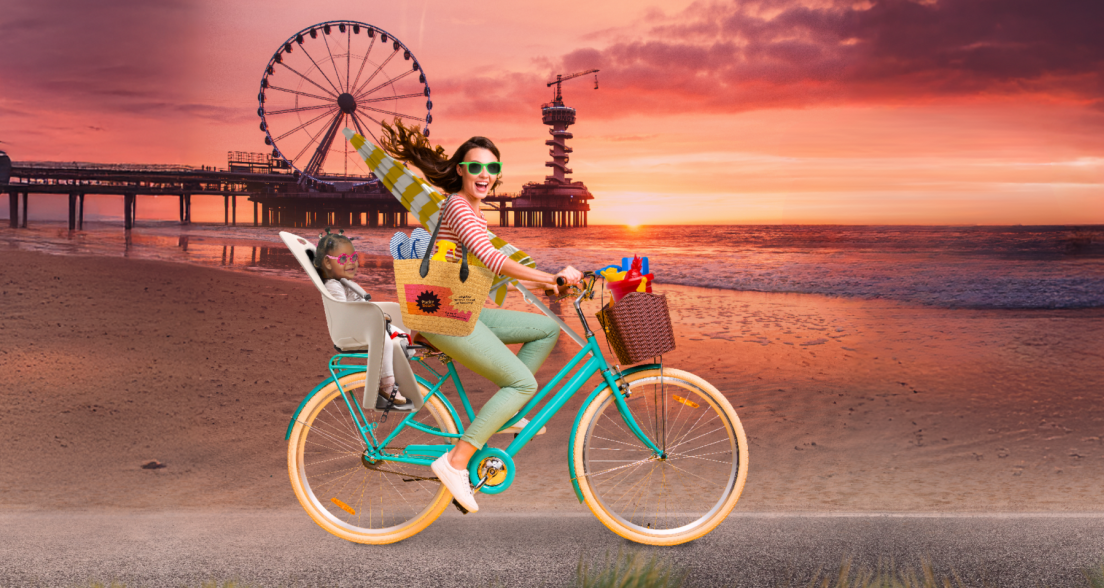 Fictief beeld van een vrouw op een fiets op het strand in Scheveningen en een kindje achterop