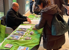 Een man geeft informatie aan een vrouw bij een stand.