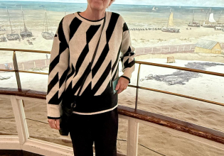 Oudere vrouw met bril en geprinte trui, voor zee schilderij.