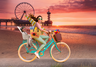 Fictief beeld van een vrouw op een fiets op het strand in Scheveningen en een kindje achterop