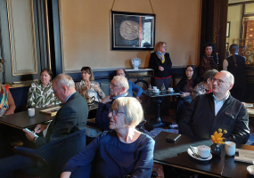 Een groep mensen zit in een café, drinkend koffie en elkaar aanstarend.