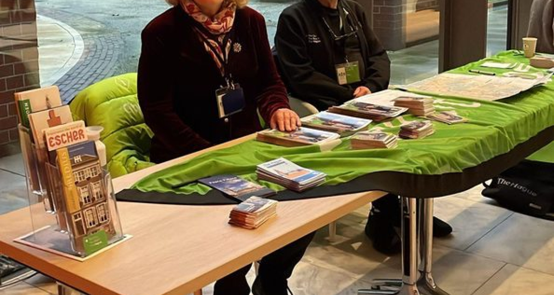 Een vrouw en een man zitten achter een tafel met brochures.