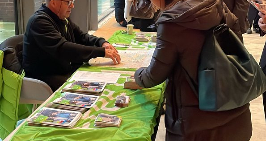 Een man geeft informatie aan een vrouw bij een stand.