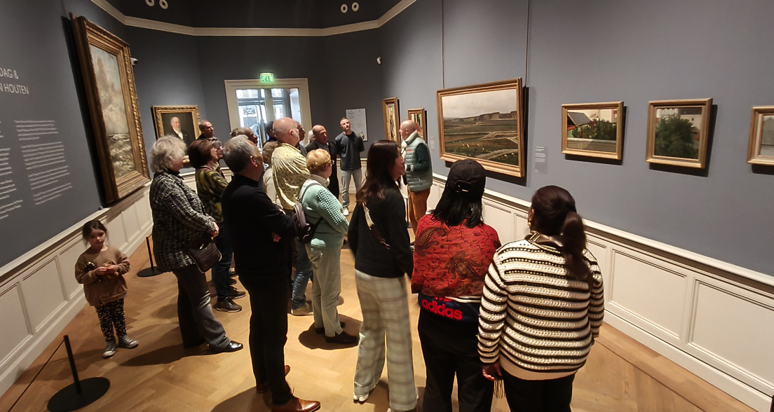 Een groep bezoekers bekijkt schilderijen in een museum.