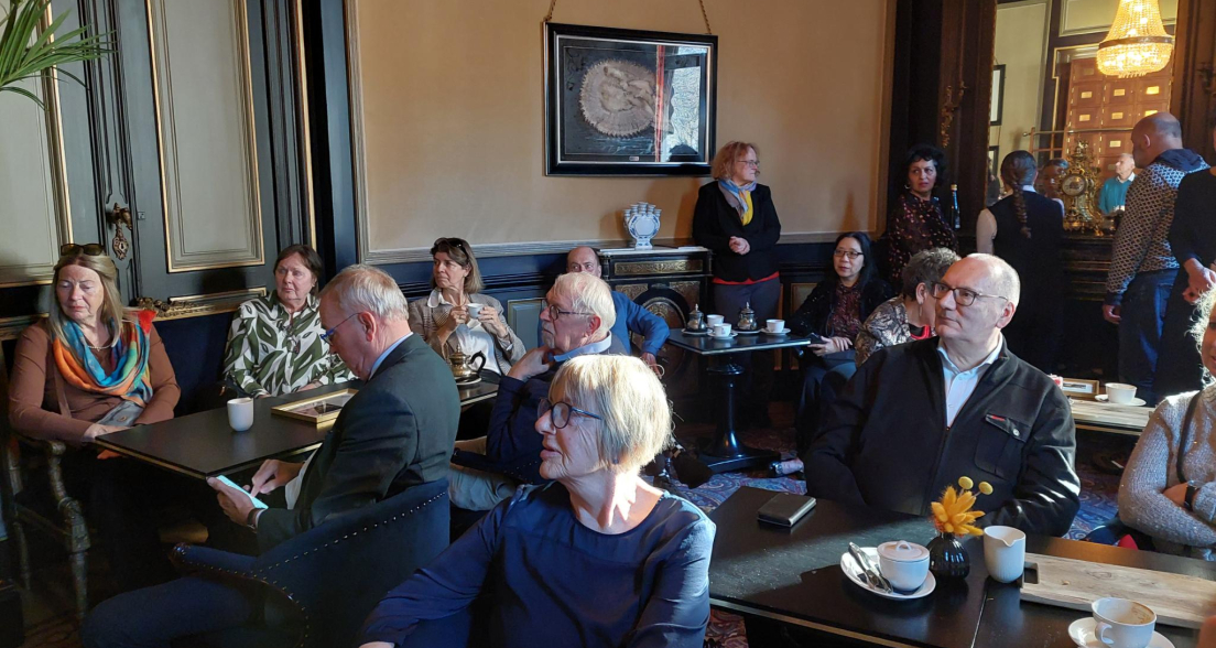 Een groep mensen zit in een café, drinkend koffie en elkaar aanstarend.
